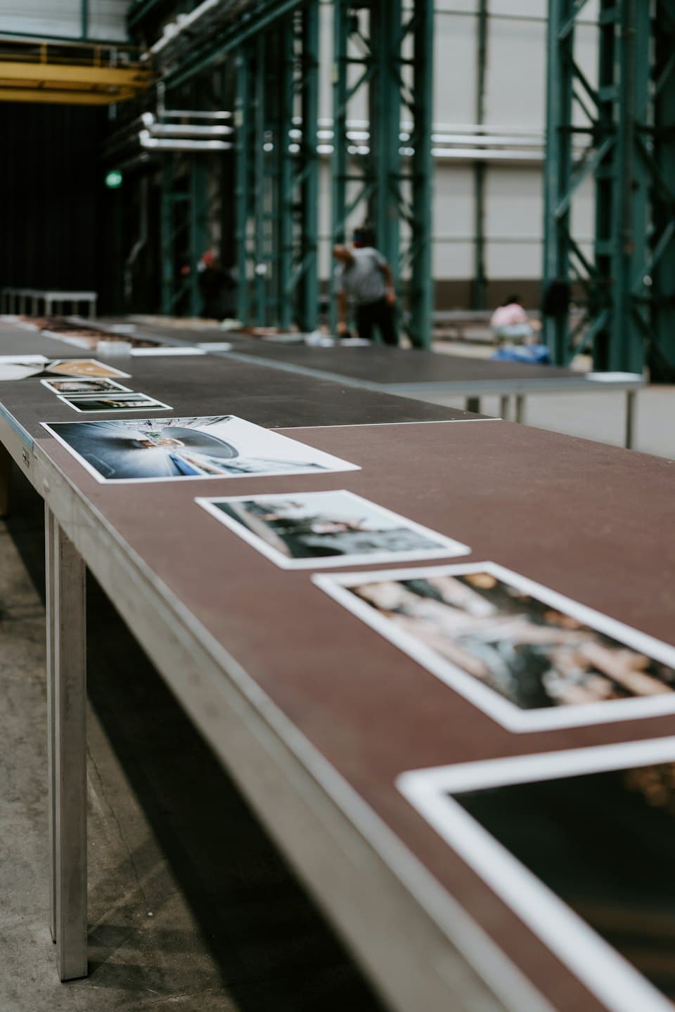 Stampe fotografiche esposte su tavoli in un ambiente di lavoro industriale.